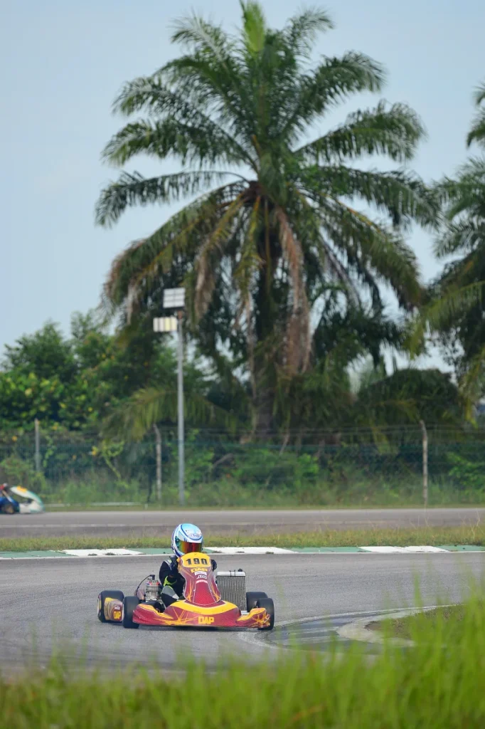 Sepang karting track turn 6 with a Junior race kart going through turn 6. Palm trees in the background.
